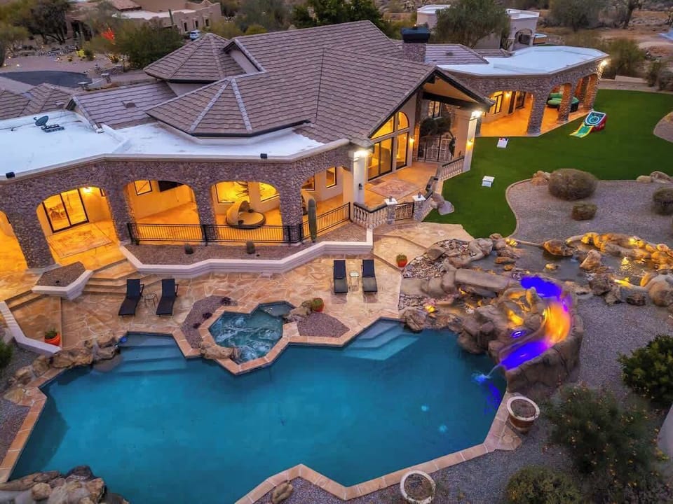 Elevated view of a luxury vacation rental featuring stunning architecture, a resort-style pool with waterfall, hot tub, spacious lawn, and children's play area.