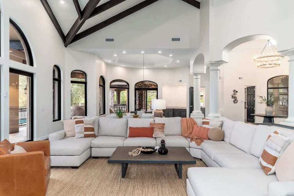 Gather your group in this stunning living space with soaring ceilings, exposed beams, and sunlight streaming through elegant arched windows. Sink into plush seating and feel right at home in this thoughtfully designed retreat.