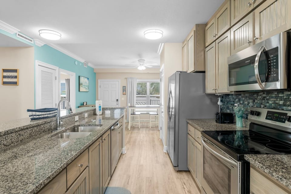 Your fully equipped galley kitchen features granite counters, stainless appliances, and coastal charm with turquoise accents throughout the open space.