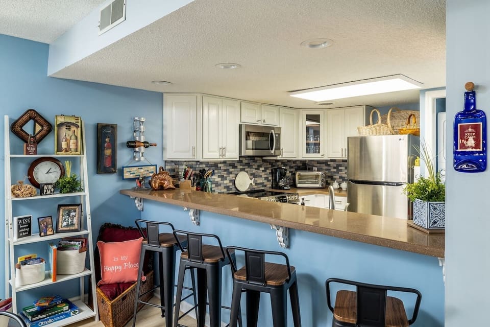 Bar looking into kitchen- 4 stools increasing dining seating to 10. Shelves containing children’s books & games