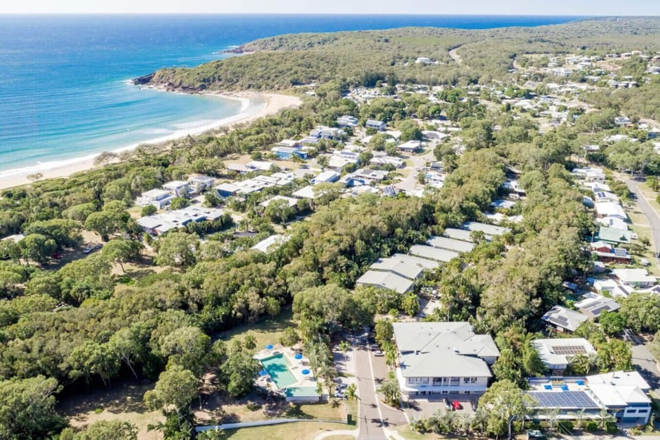 Aerial coastal town with sandy beach, ocean bay, and lush surrounds. Family‑friendly destination with natural light and inviting scenery.