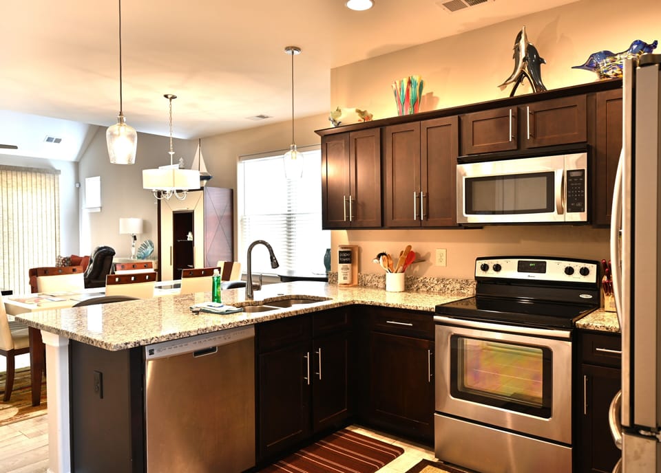 Modern kitchen with granite, dark wood & pendant lights by bright living.
