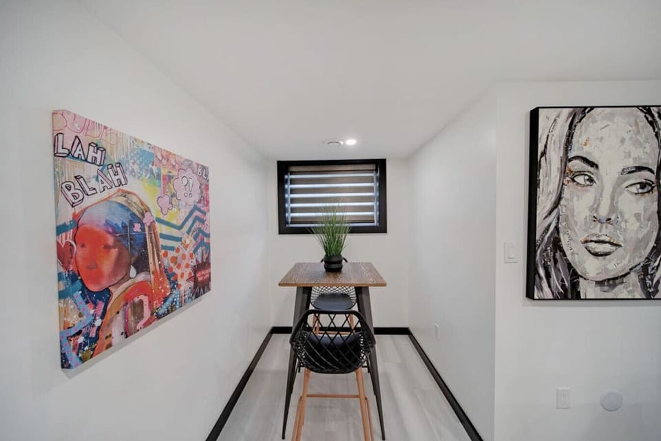 Cozy dining area with a high-top table and stylish bar stool. Features vibrant wall art, a large portrait, and a window with blinds. Perfect for intimate meals or working. Modern design & artistic touches for your stay.