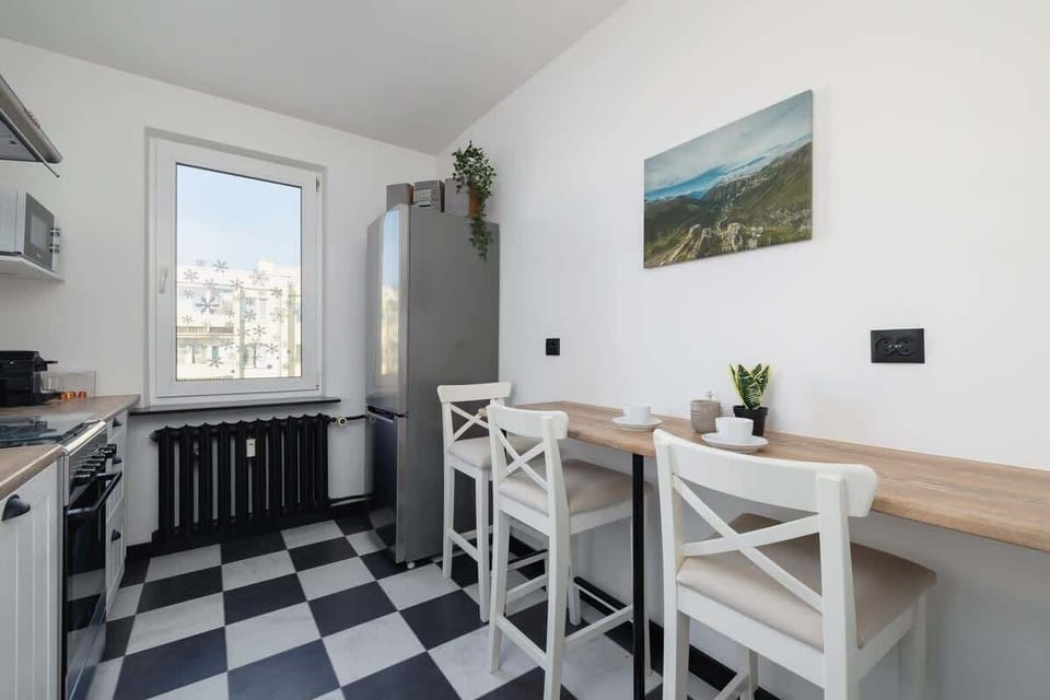 Compact kitchen with dining area, checkered floor, and a window with city views.
