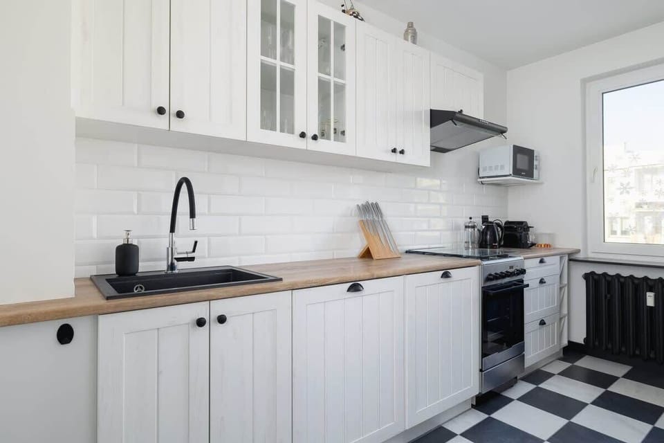 Kitchen with white cabinets, checkered floor, and wooden countertop.
