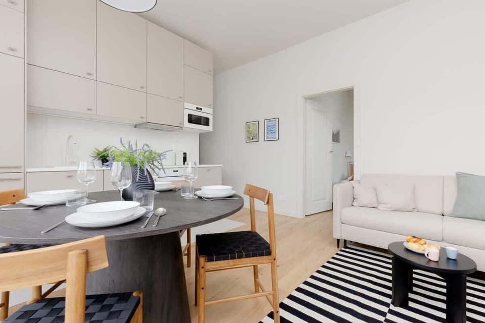 Combined living and dining space with white cabinetry, round table, and the same striped rug.

