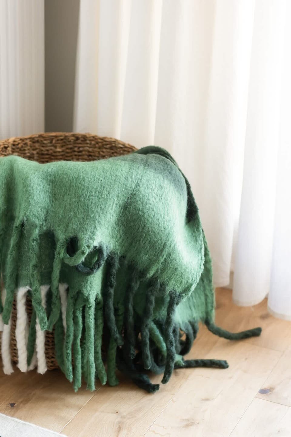 Green throw blanket folded neatly on a stool near a sunlit window.
