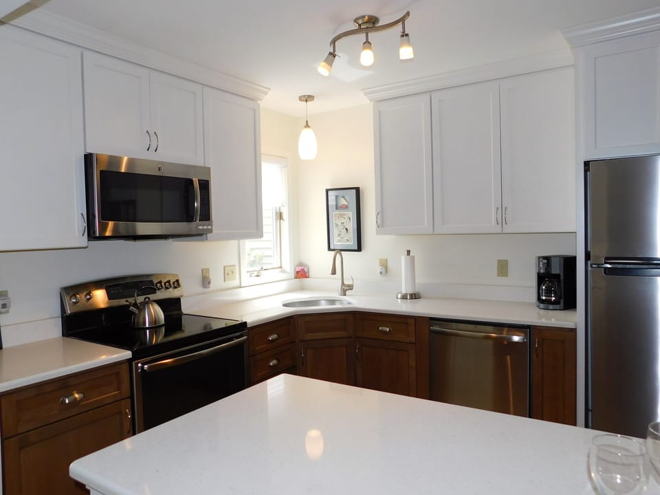 543C hudspn Ave, Stewards Watch, Bethany Beach - The kitchen has been fully modernized with a two-tone cabinetry style—clean white uppers and warm wood-toned lowers—paired with stainless steel appliances and white quartz countertops. The open-concept layout includes a breakfast bar that looks through to the dining area, creating a social flow that is highly desirable for coastal living.