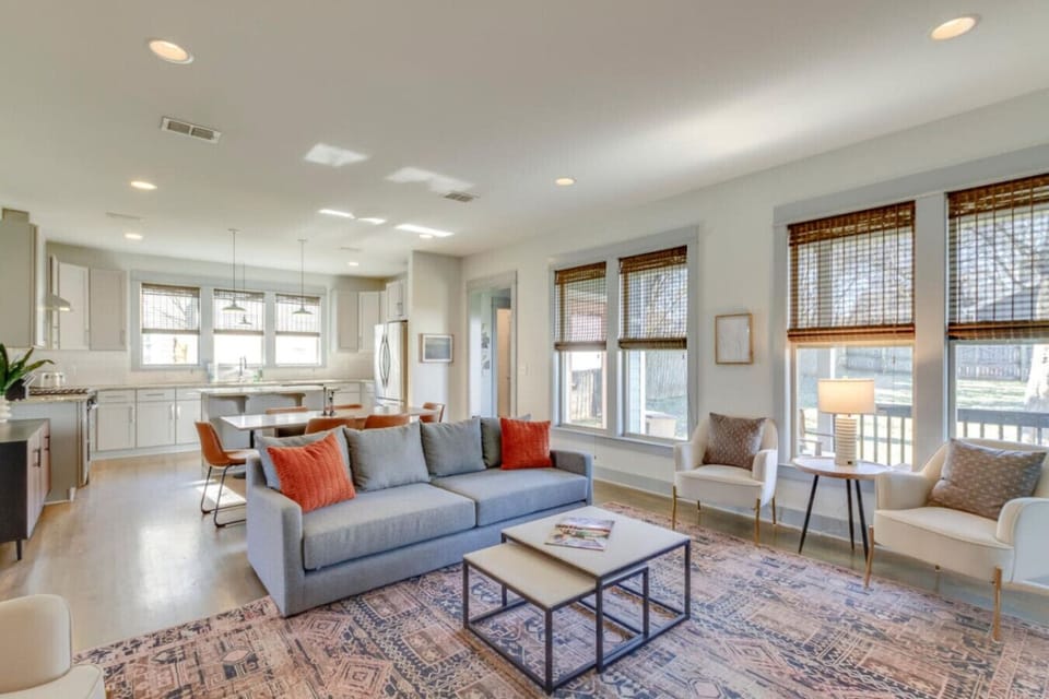 A bright and spacious living room with gray sofas, orange accent pillows, and large windows feels welcoming.