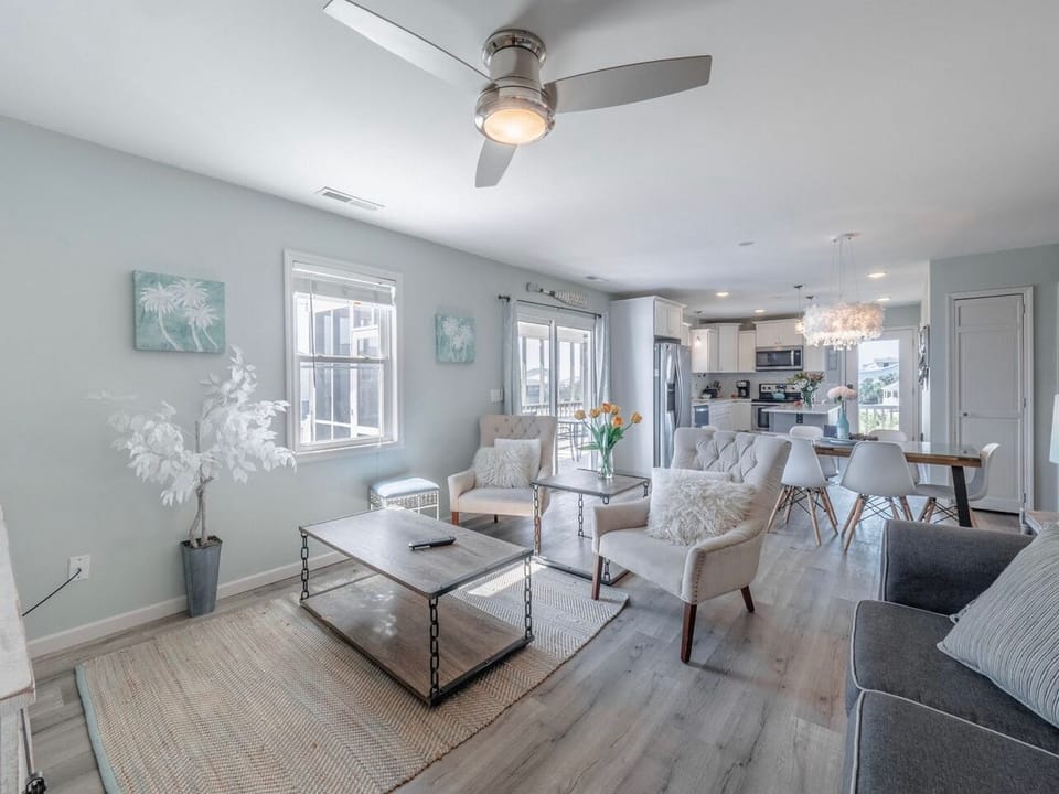 Bright living room with comfortable sofa, large TV, coffee table, and coastal décor, plus windows bringing in natural light and easy access to nearby bedrooms in this Oak Island beach home.