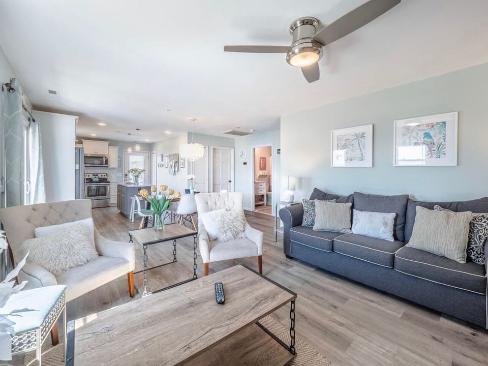 Bright living room with comfortable sofa, large TV, coffee table, and coastal décor, plus windows bringing in natural light and easy access to nearby bedrooms in this Oak Island beach home.