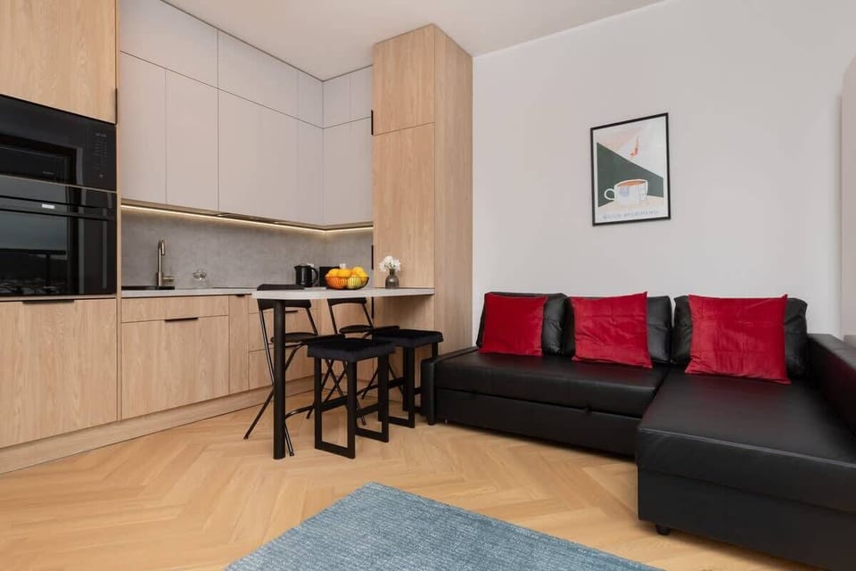 Open-plan kitchen and living area with black sofa and bright natural light.
