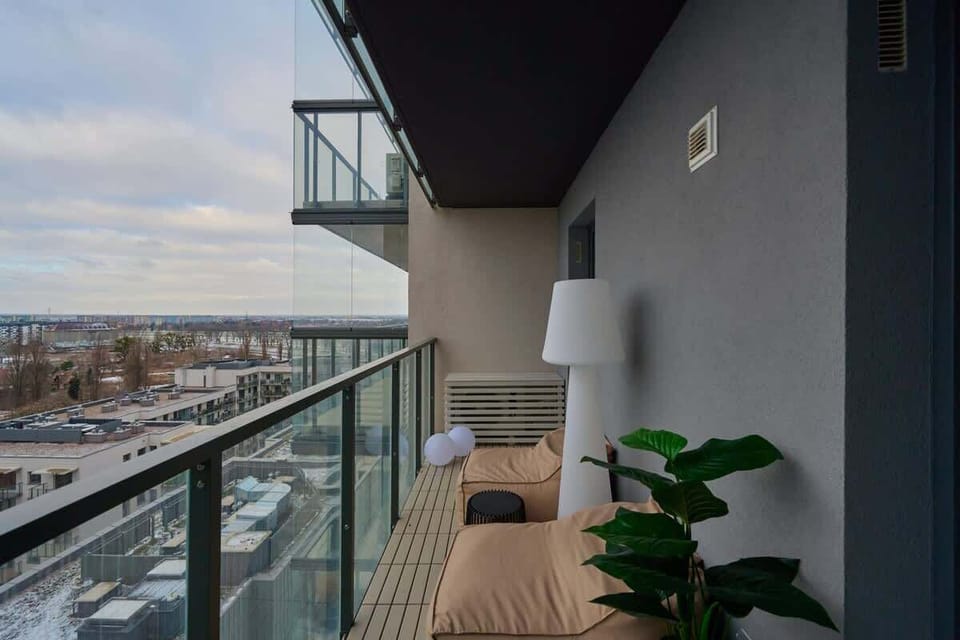 Balcony with glass railing, potted plants, and panoramic city view.
