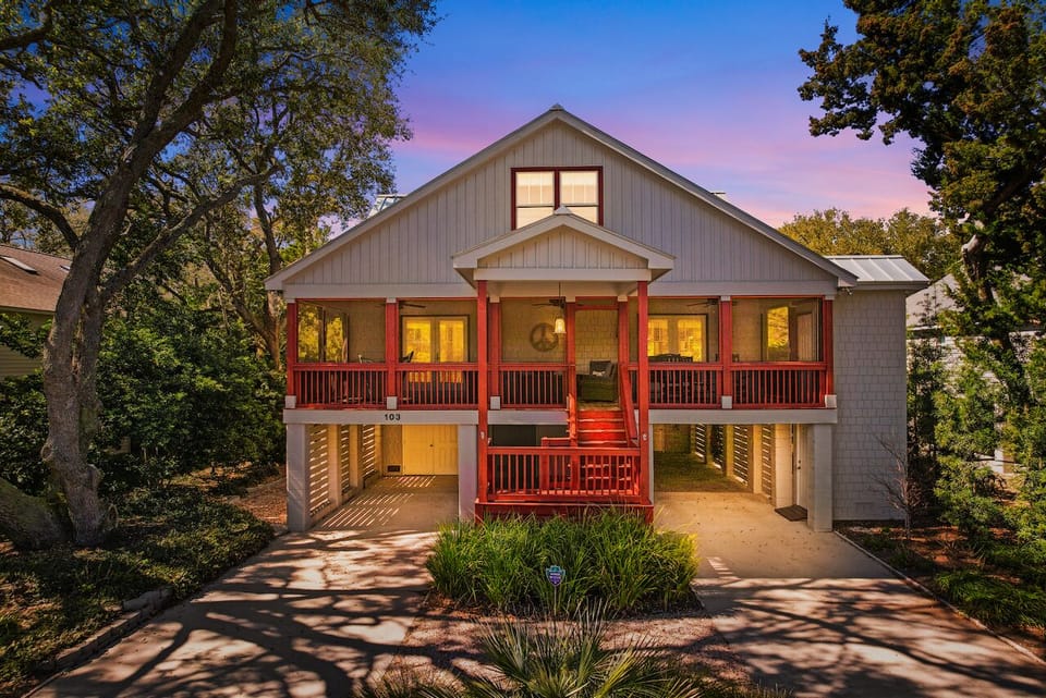 Charming coastal cottage with warm evening glow, featuring wraparound porches and mature trees creating a peaceful neighborhood setting.