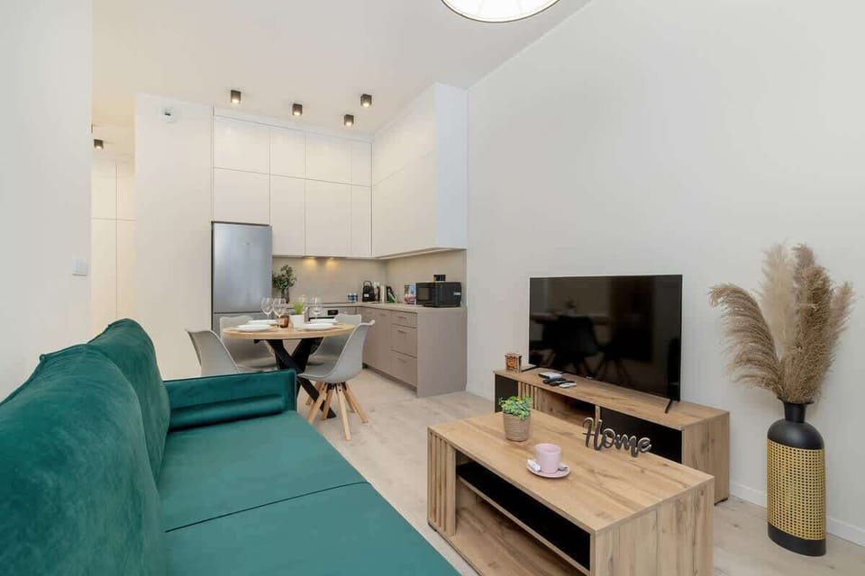 Living area with green sofa, wooden TV unit, and decorative pampas grass.
