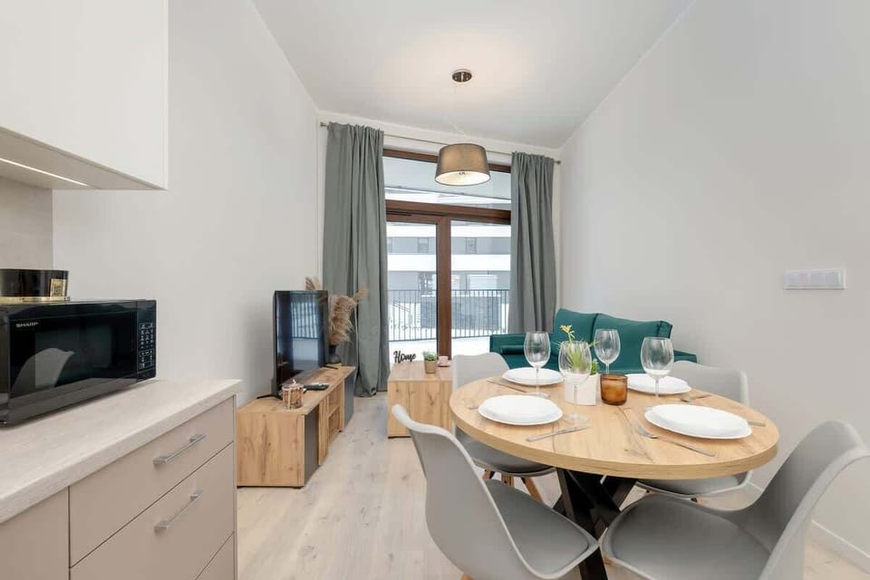 Dining area with round table, green chairs, and floor-to-ceiling window.
