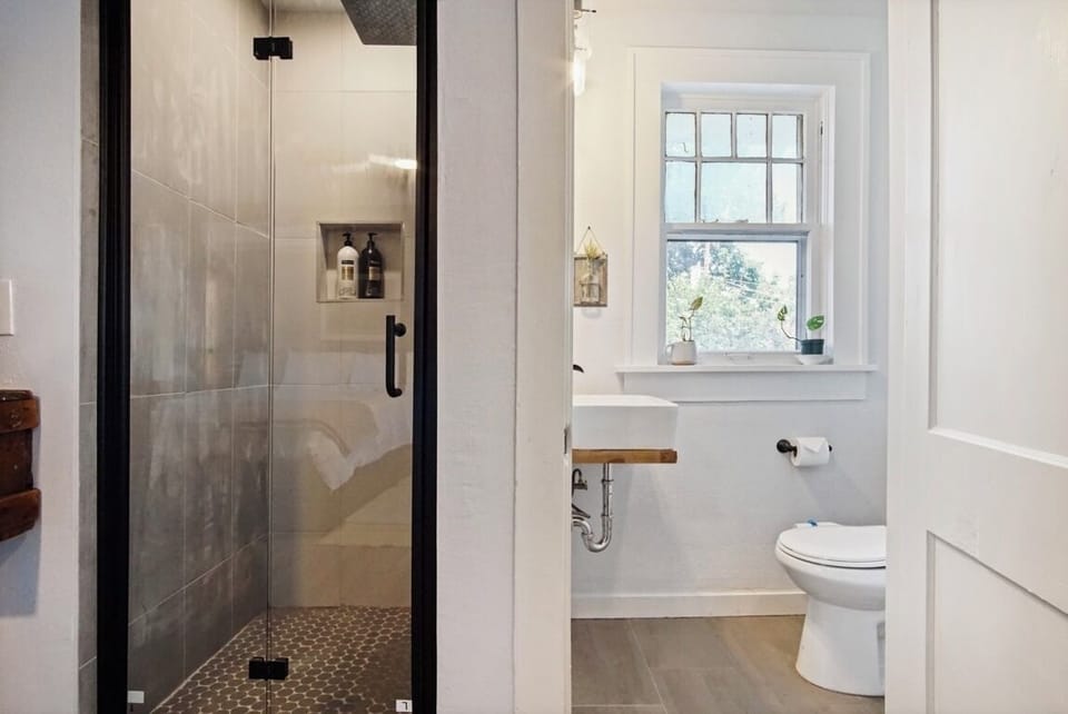Bright, modern bathroom with walk-in glass shower and natural light from a charming window.



