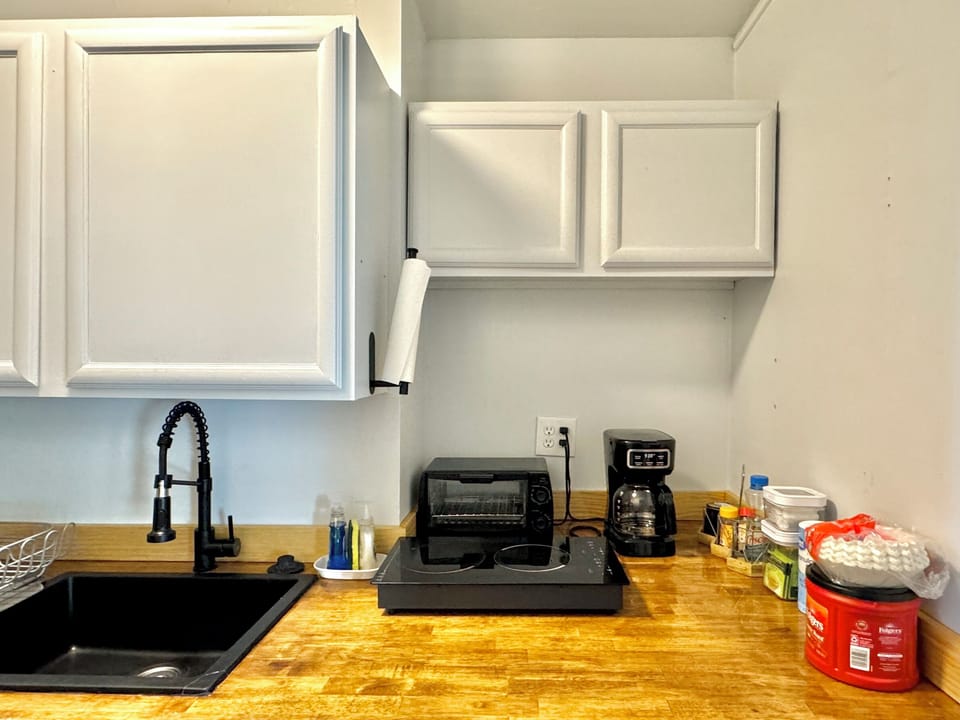 Compact Kitchenette — Butcher block counters with black sink, toaster oven, coffee maker, and essential condiments for quick, easy meals.