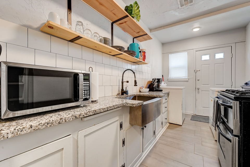 Charming kitchen with farmhouse sink, granite counters, and open shelving for a stylish, functional touch.
