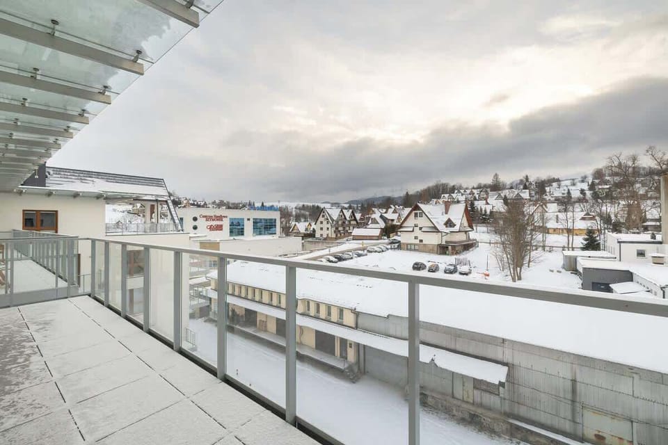Balcony with glass railing offering a wintery cityscape view.
