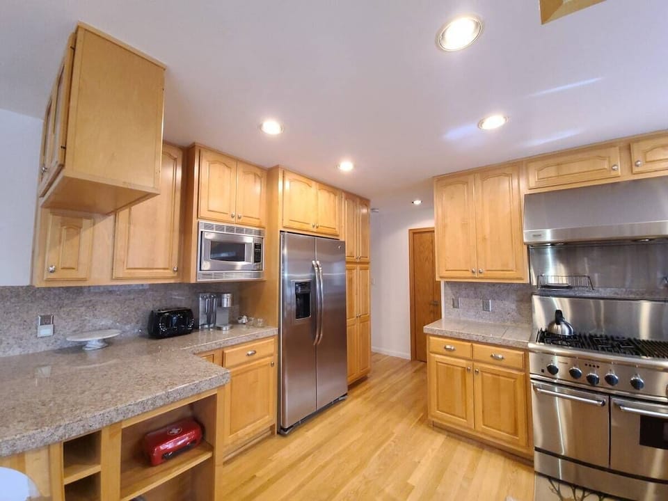 Kitchen with refrigerator, microwave, range, cabinets, blender, counter, and door.