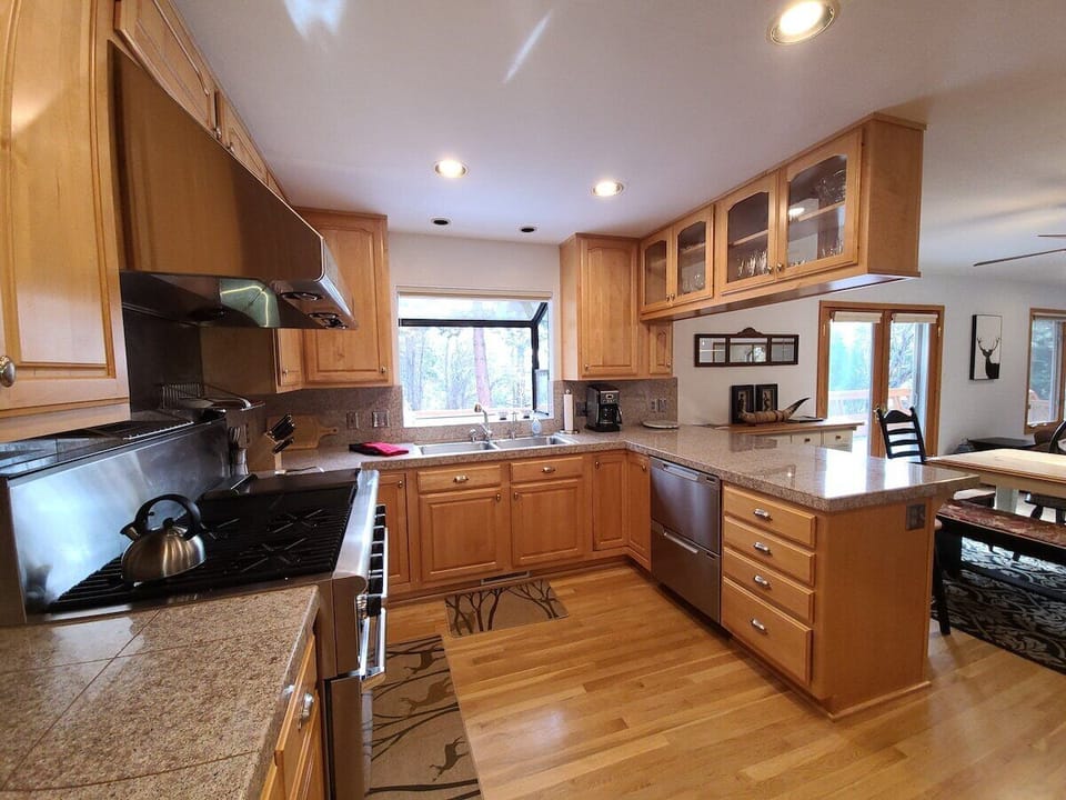 Kitchen with range, sink, dishwasher, coffee maker, cabinets, breakfast bar, windows, sliding doors, dining table, and chairs.