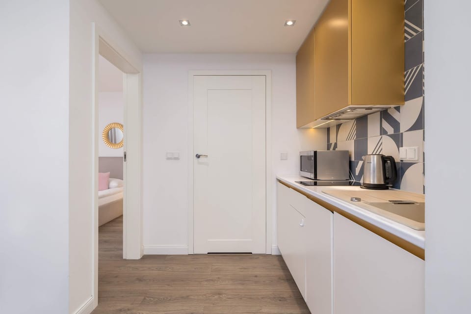 Modern kitchen with gold upper cabinets, sleek white surfaces, and a floral backsplash.
