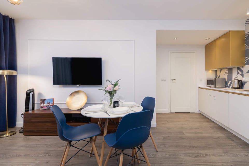 Open-plan space with a mounted TV, chic dining set, and bright modern kitchen.
