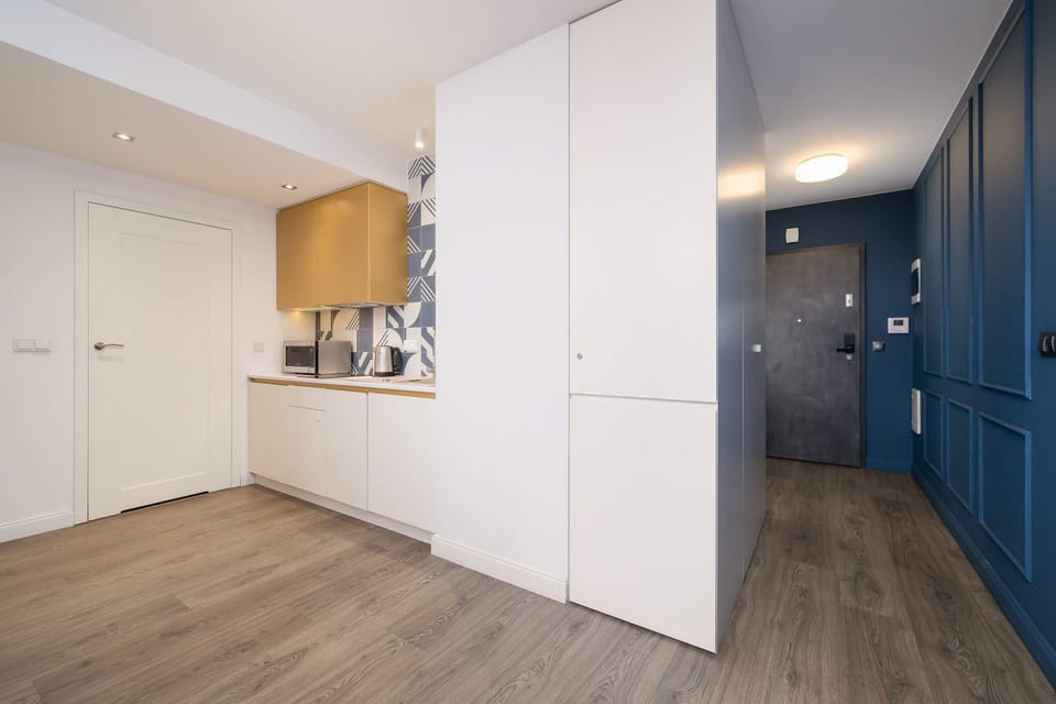 Sleek kitchen hallway with white cabinets, wooden flooring, and blue paneling.
