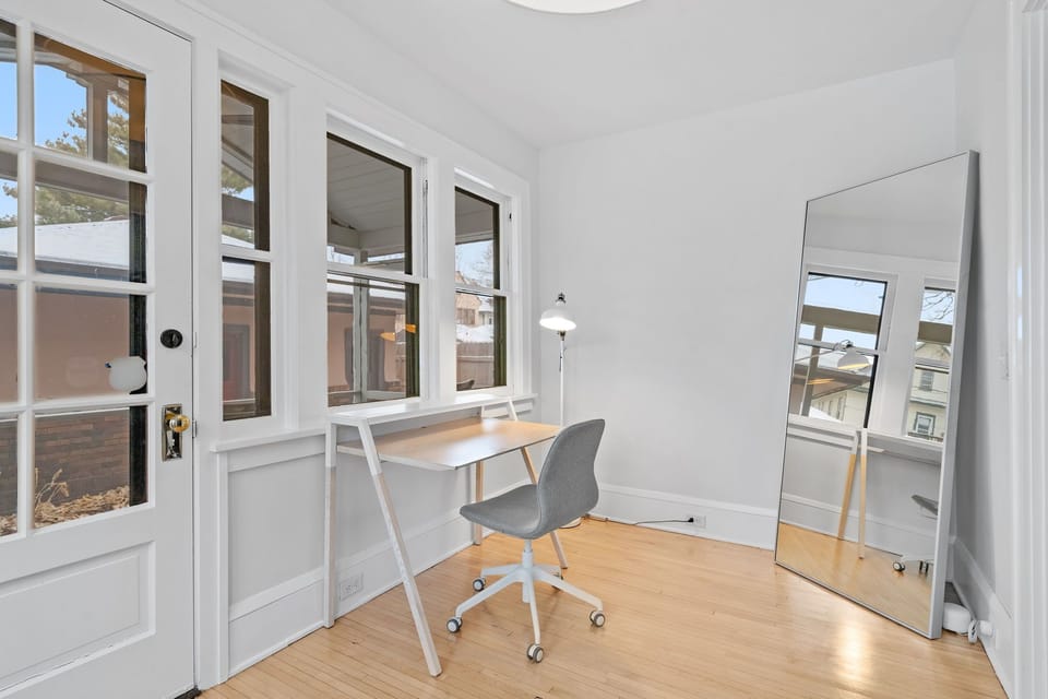 Your bright workspace features a sleek desk, ergonomic chair, and floor-to-ceiling mirror, creating an inspiring environment for productivity.