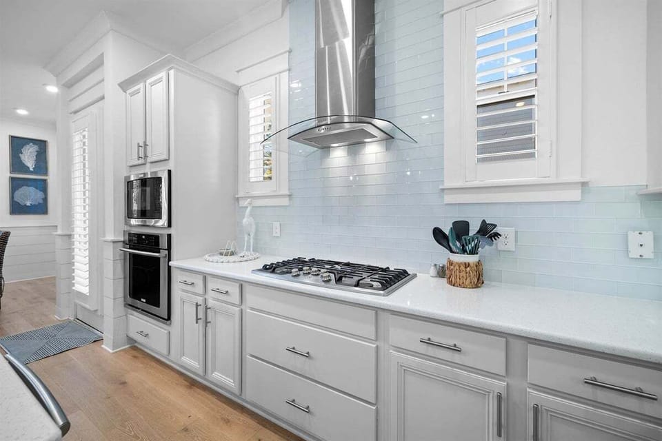 A bright and well-organized kitchen with white cabinetry, stainless steel appliances, and a beautiful backsplash.