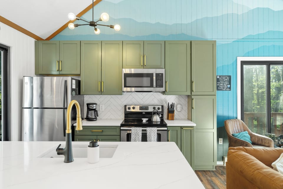 Stylish kitchen with sage cabinets, quartz island & forest-view deck