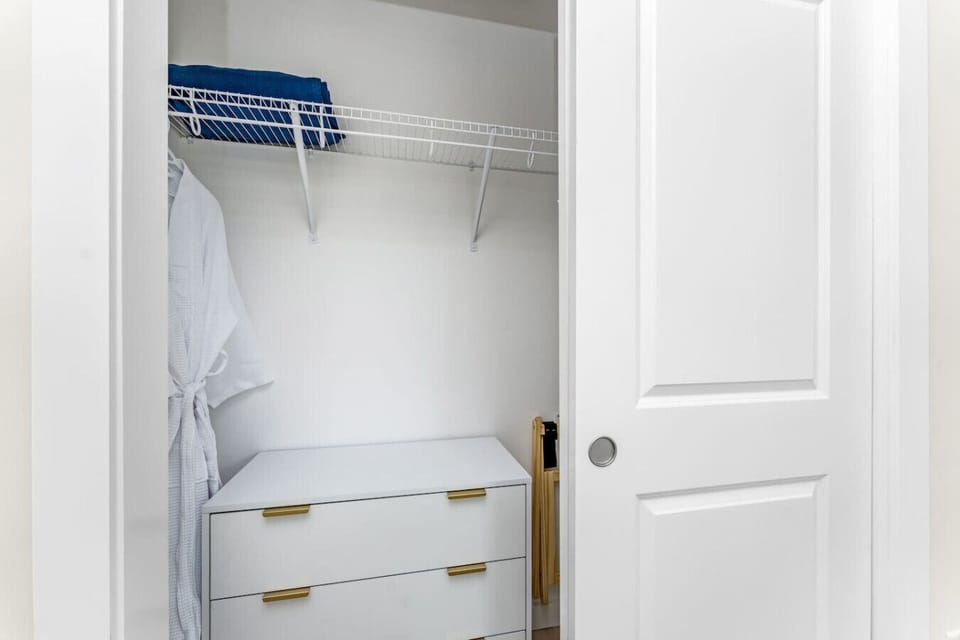 Bedroom closet with dresser drawers, hanging space with hangers, robes, extra linens, and a luggage rack for convenient storage during your stay.