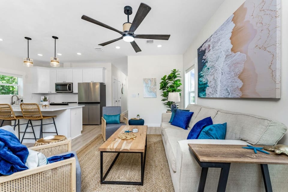 The open-concept living room and kitchen in Unit 1A create a bright, comfortable space with coastal décor, stainless steel appliances, bar seating, and a queen sofa sleeper—perfect for relaxing after a day at the beach.