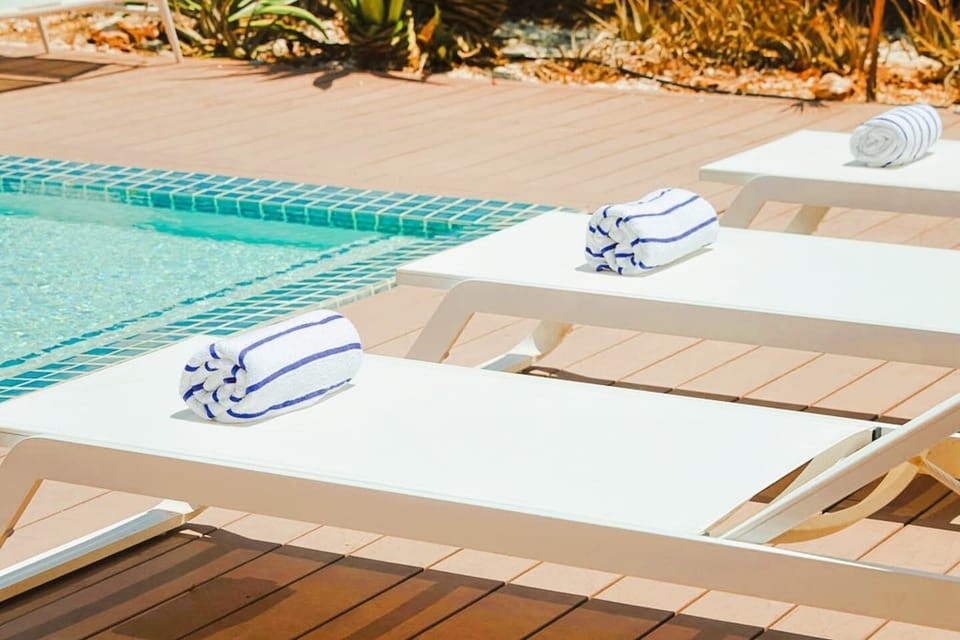 A large private pool glistens beside an expansive terrace, complete with sun loungers, shaded lounge seating and a bespoke artisan dining table designed for long, memorable meals in the tropical breeze.