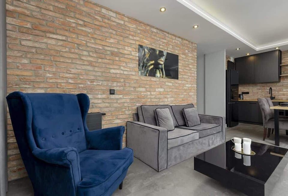 Industrial-style living area with exposed brick walls, a plush blue armchair, and cozy gray sofas.
