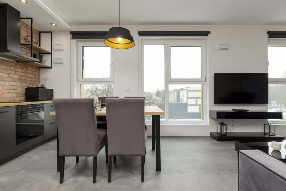 Elegant dining setup with a dark wooden table, plush gray chairs, and a striking black-and-gold pendant light.
