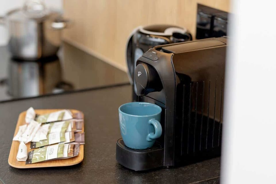 Compact coffee station with a black espresso machine, a blue cup, and a selection of teas.
