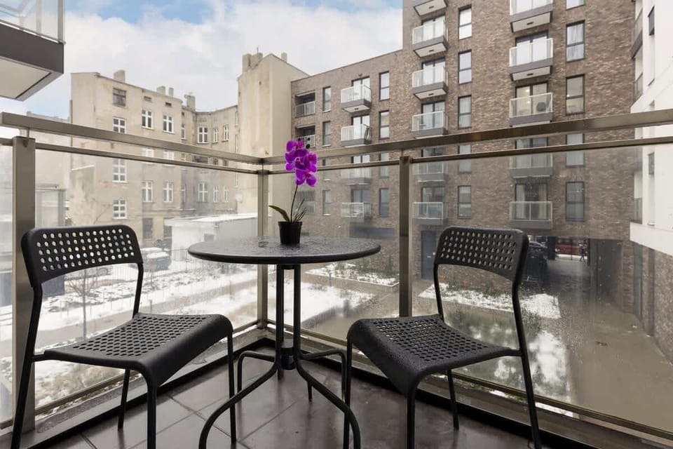 Cozy balcony with a black metal table and chairs, overlooking an urban cityscape.
