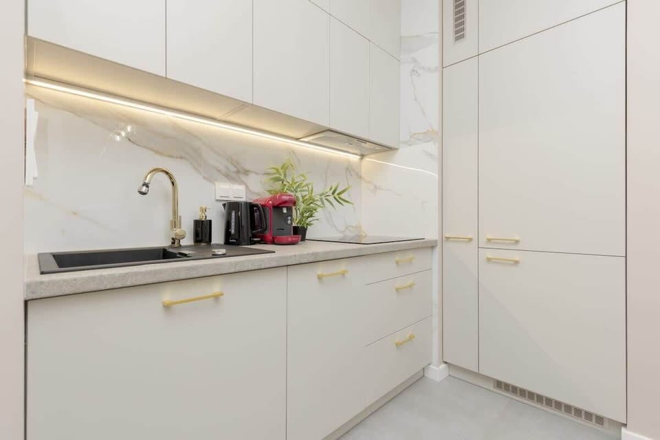 Modern kitchen with white cabinetry, gold handles, and under-cabinet lighting.
