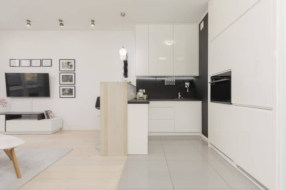 Bright open kitchen with glossy white cabinets, a black countertop, and stylish pendant lighting.
