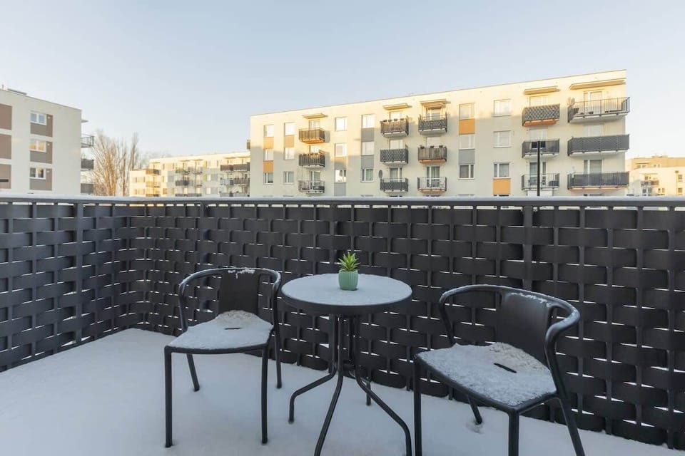 Snow-covered balcony with a black woven privacy screen, a modern table, and stylish chairs.
