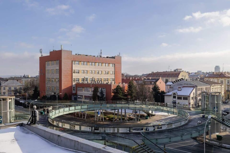 A panoramic view of a historical city square with a circular modern glass-roofed structure, harmonizing old and new architecture.
