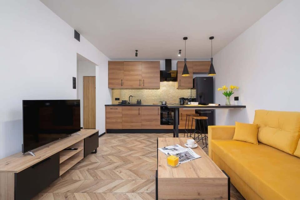 A cozy and contemporary living room with a mustard yellow sectional sofa, a wooden coffee table, and a wall-mounted TV, creating a warm atmosphere.
