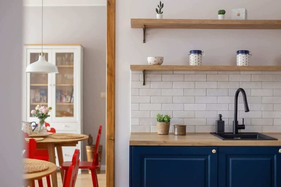 A close-up of a modern kitchen wall with open shelving, navy blue cabinets, and a sleek black faucet complementing the white subway tiles.

