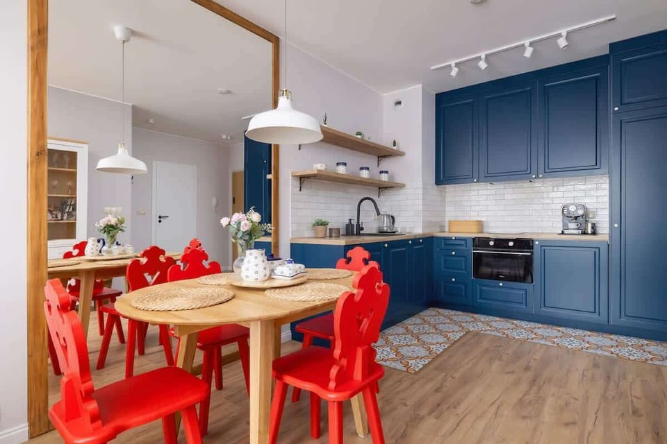 A spacious kitchen and dining area with deep blue cabinets, bright white countertops, and striking red chairs adding a lively contrast.


