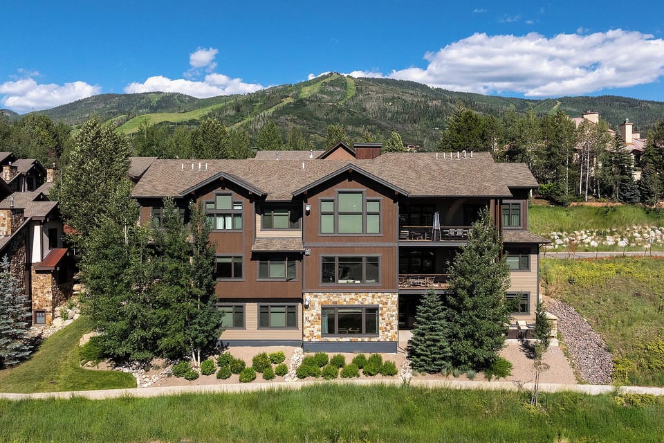 Mountain lodge nestled in a scenic valley with forested peaks and blue skies creating a perfect alpine retreat setting.