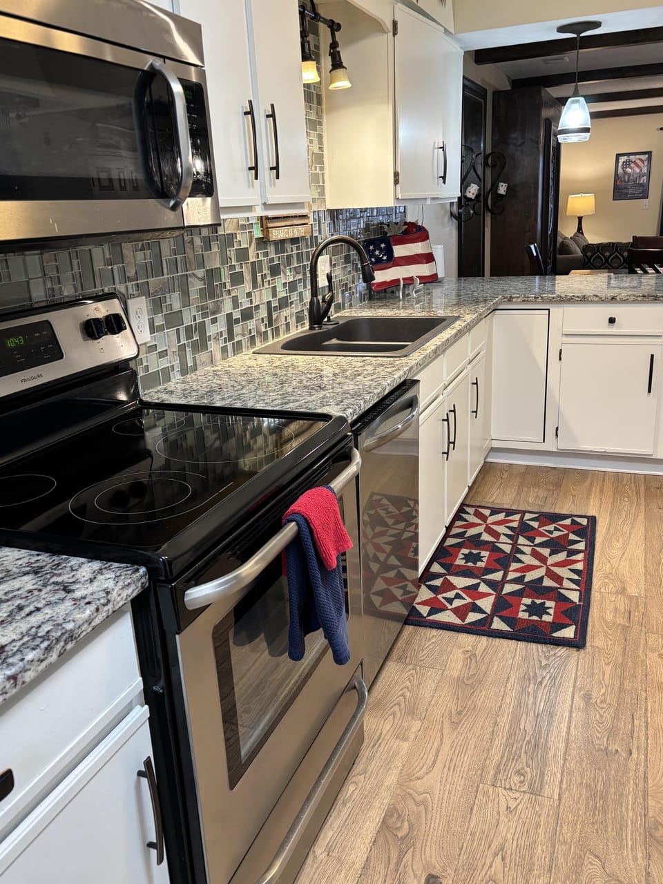 Kitchen features stainless steel appliances, white cabinetry, granite countertops, mosaic tile backsplash, and wood-look flooring.