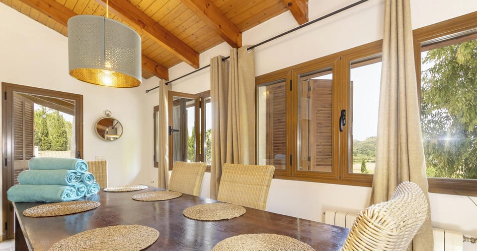 View of the indoor dining area at Villa Alejandra featuring a large wooden table, natural fibre chairs, wooden beam ceiling and large windows overlooking the natural surroundings.