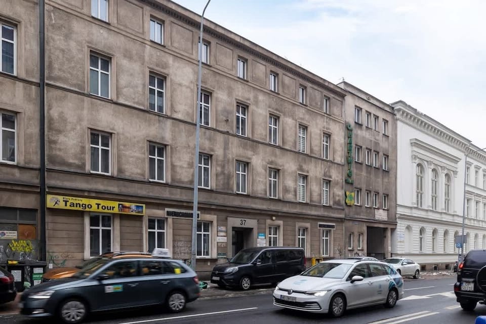 A lively street view featuring classic European-style buildings, cars parked along the road, and various shops, offering a glimpse of the neighborhood's charm and character.






